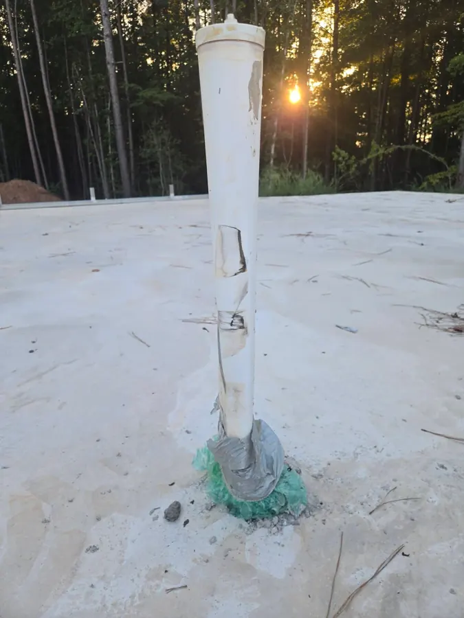 Large white PVC plumbing pipe coming up through the slab, leaning, with black scuff marks and gouges along its side
