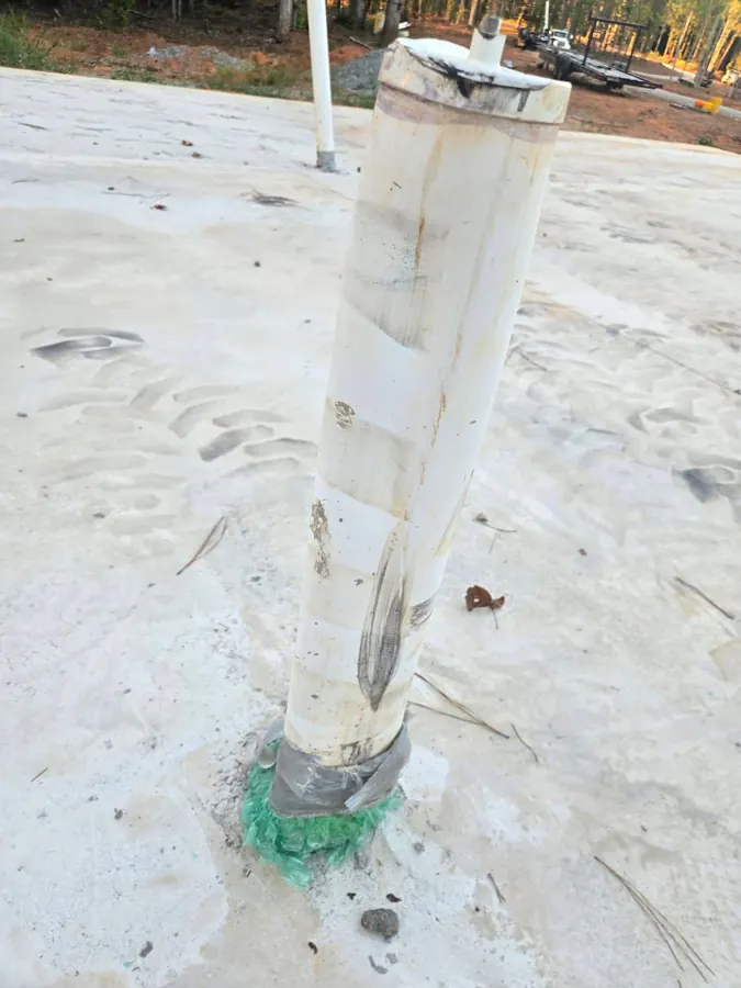 Close view of a scuffed and gouged PVC pipe in the slab with equipment tire tread marks on the concrete around it