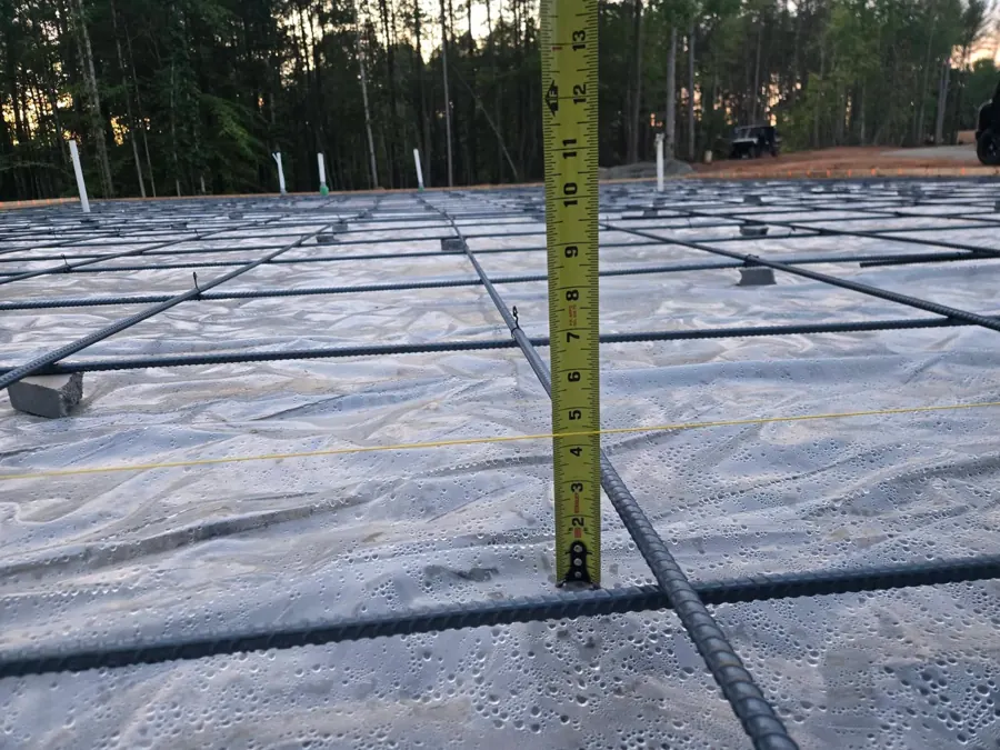 Tape measure standing on the vapor barrier of a rebar-reinforced slab before the pour, with a yellow string line crossing the tape at about four and a half inches